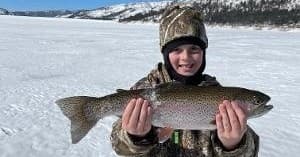 Child holding large trout on snowy frozen lake ice