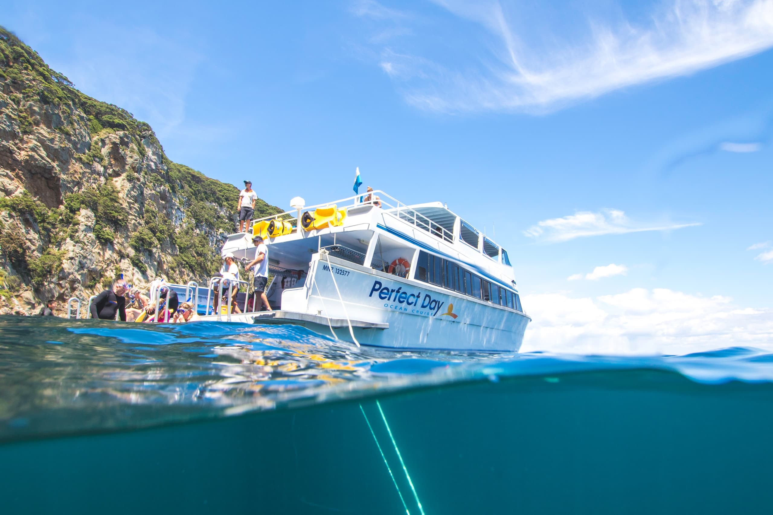 Dive boat with passengers cruising near rugged coastal islands, NZ