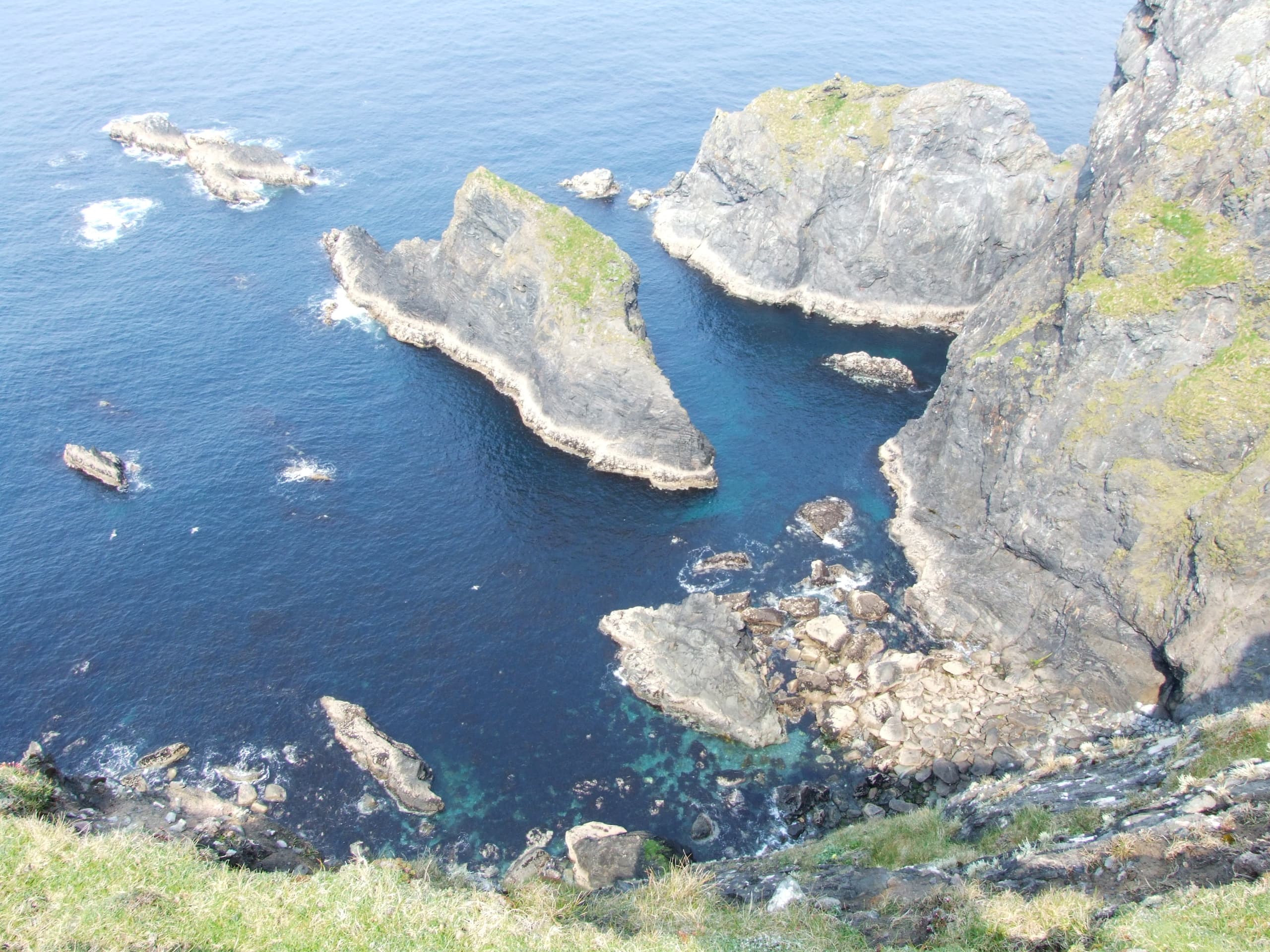 Aerial cliffside coastal rocks and clear blue sea views