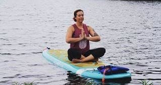 Woman meditating on a paddleboard in peaceful lake waters