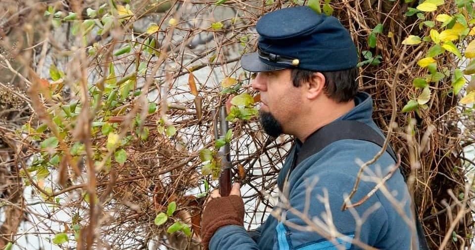 Civil War reenactor peering through brush on wooded skirmish
