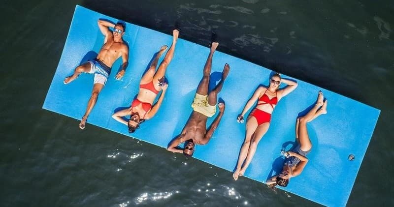 Group relaxing on floating water mat in sunlit open water