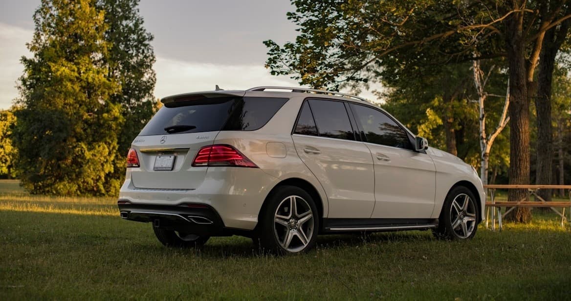 White SUV parked on grassy meadow near trees for scenic countryside drive
