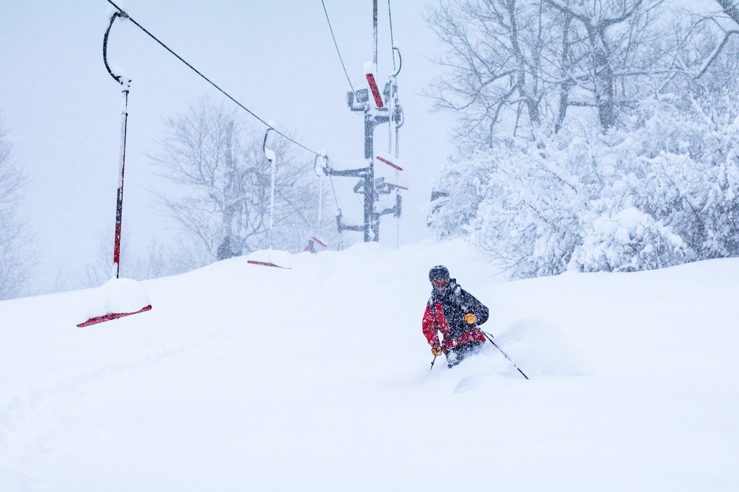 Skier descending snowy run beneath chairlift in heavy snow