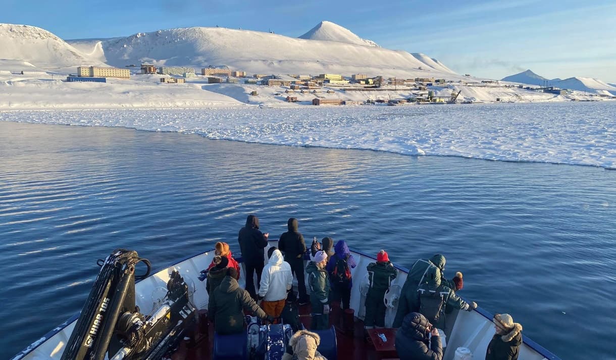 Passengers aboard expedition ship approaching snowy Svalbard settlement