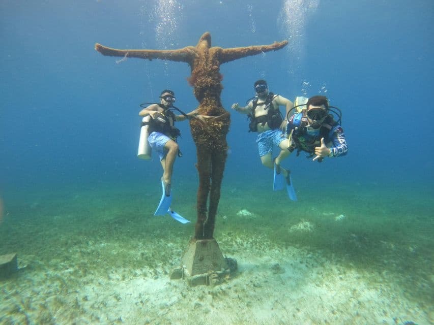 Scuba divers exploring submerged statue monument on reef in Cozumel