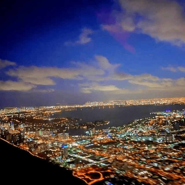 Night aerial helicopter tour over illuminated coastal city and bay