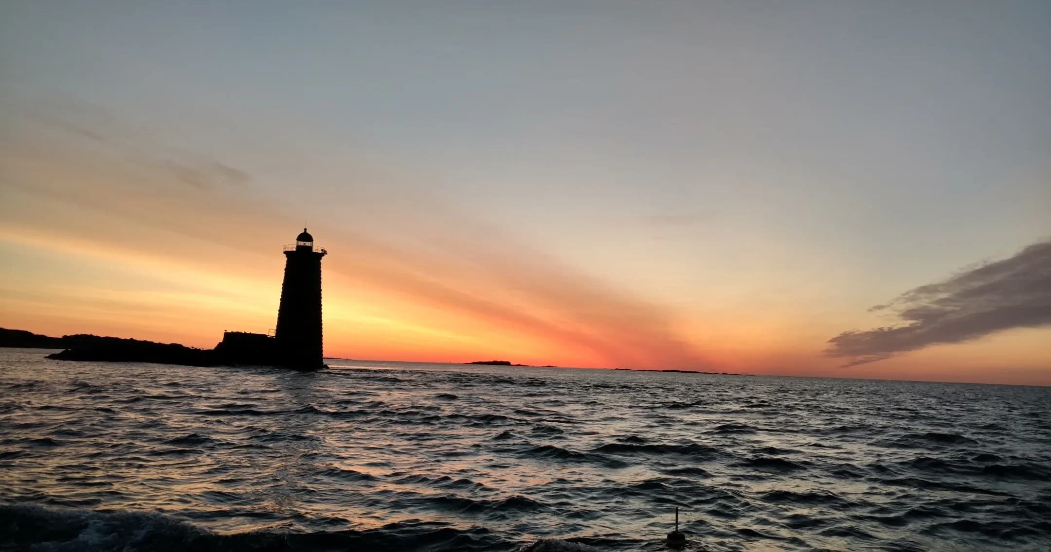 Sunset lighthouse silhouette over choppy Atlantic ocean near shore