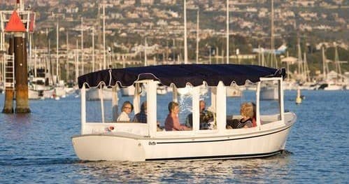 Sightseeing boat on calm Newport Beach bay with seated passengers