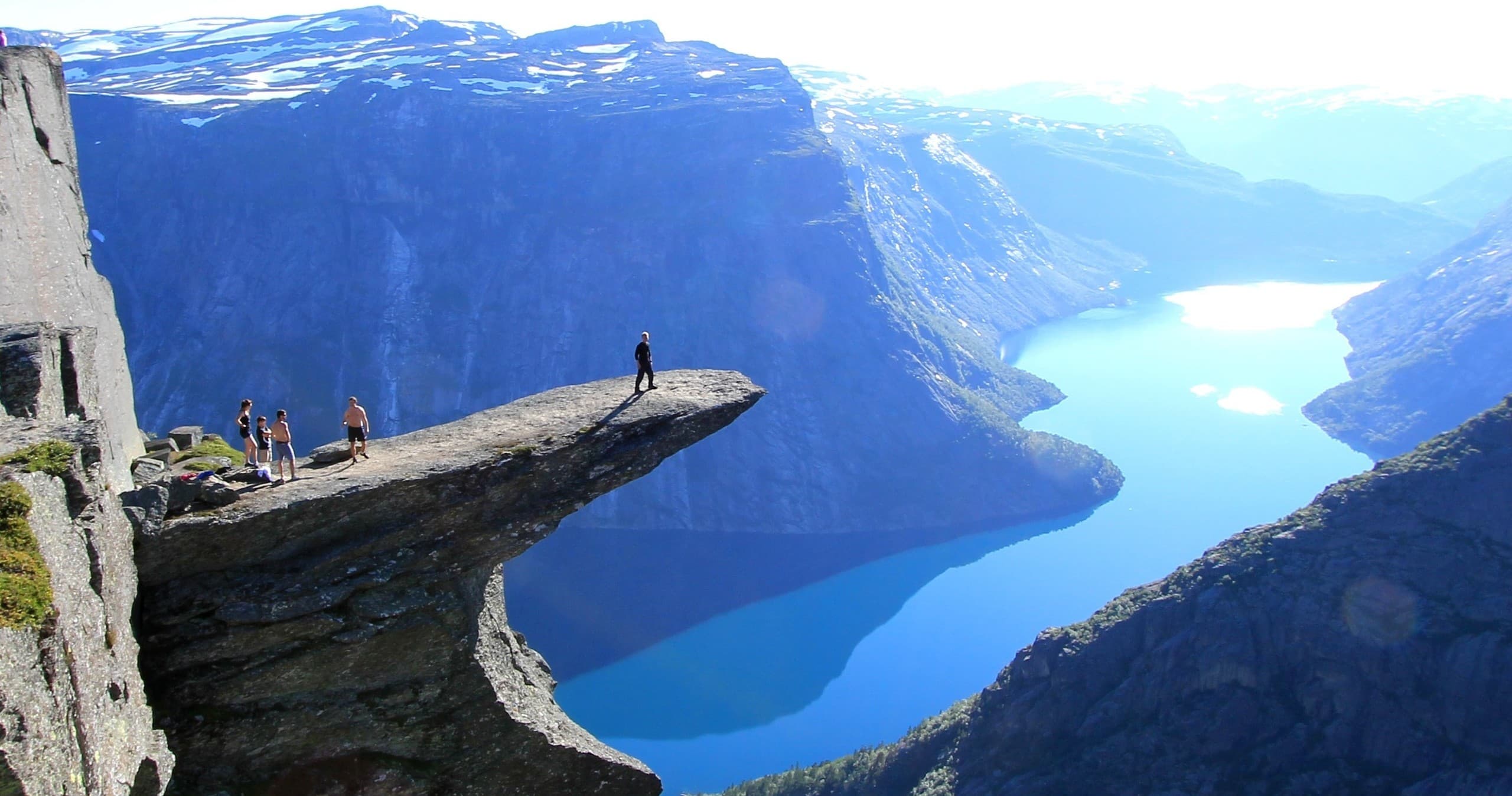 Hikers on dramatic rock ledge overlooking blue fjord at Trolltunga