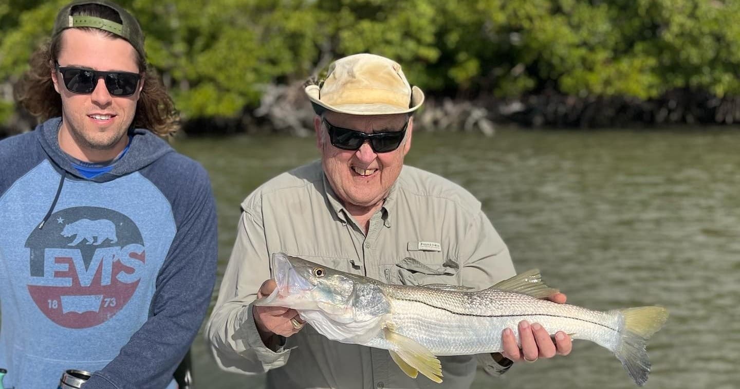 Two anglers holding snook near mangrove shoreline on flats