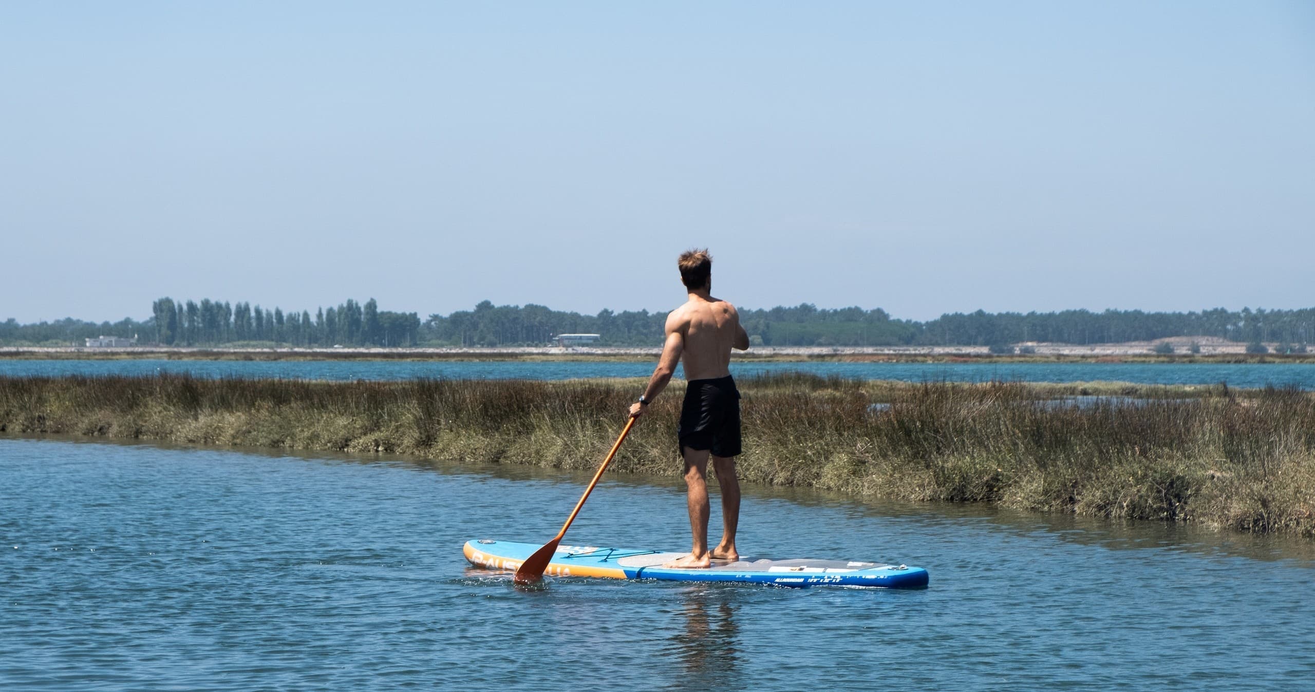 Stand-up paddleboarder exploring calm coastal marshes at sunset
