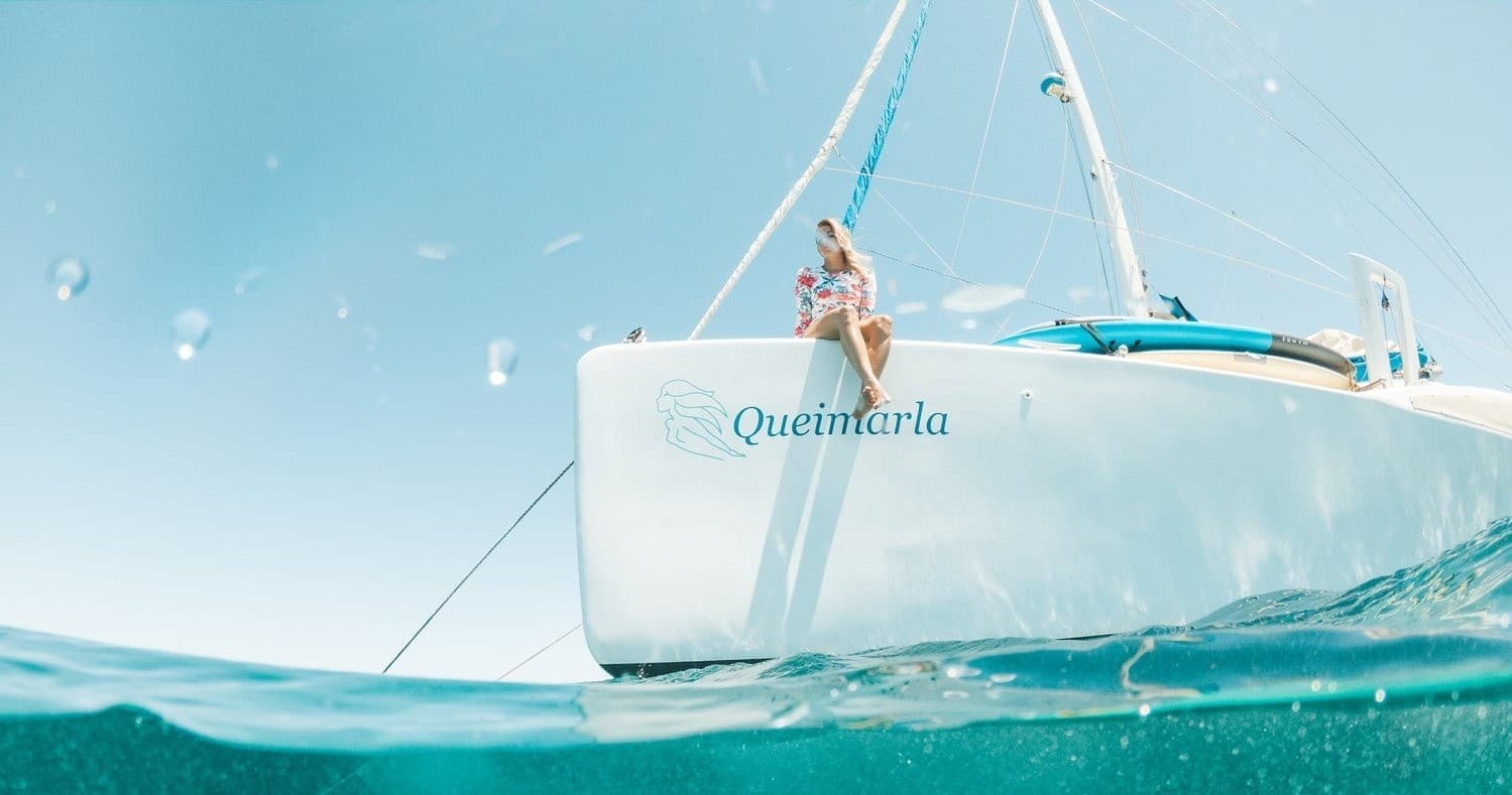 Catamaran on turquoise sea with passengers on bow enjoying swim