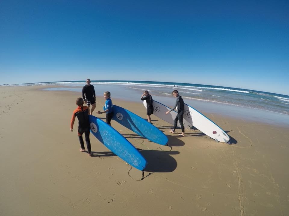 Surf school group with boards on sandy ocean beach at sunrise