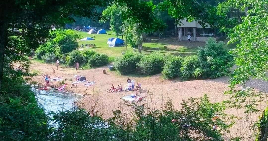 Riverside sandy beach campsite with tents and swimmers