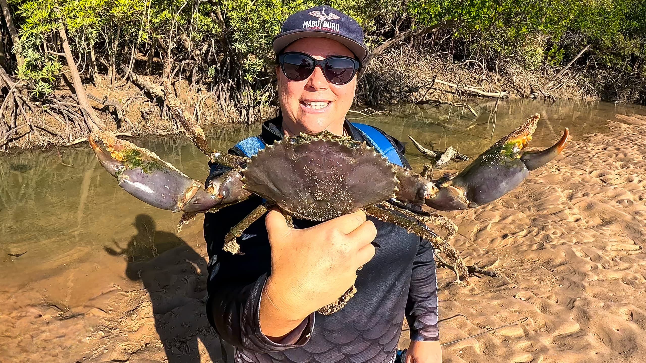 Angler holding large mud crab on riverbank during low tide