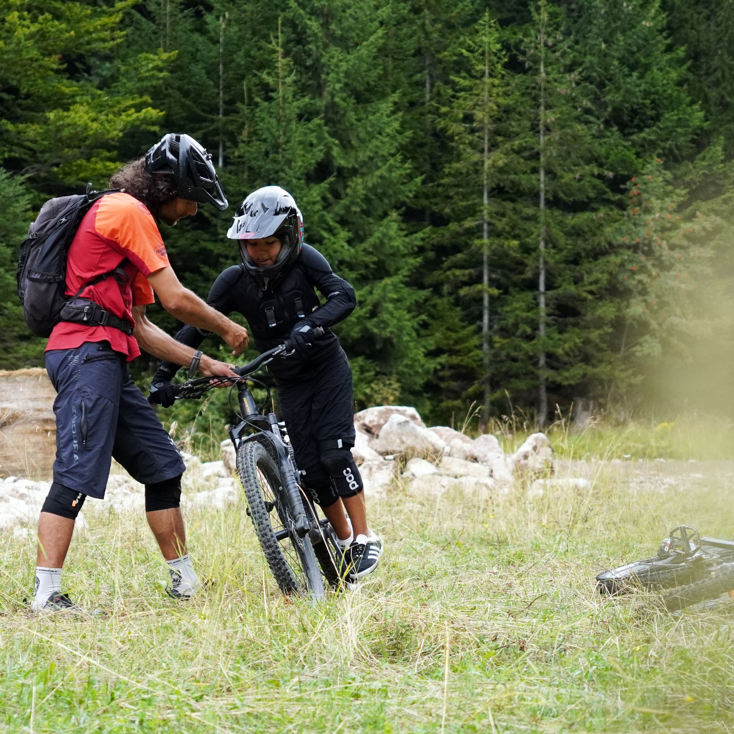 Instructor coaching child mountain biker on grassy trail edge