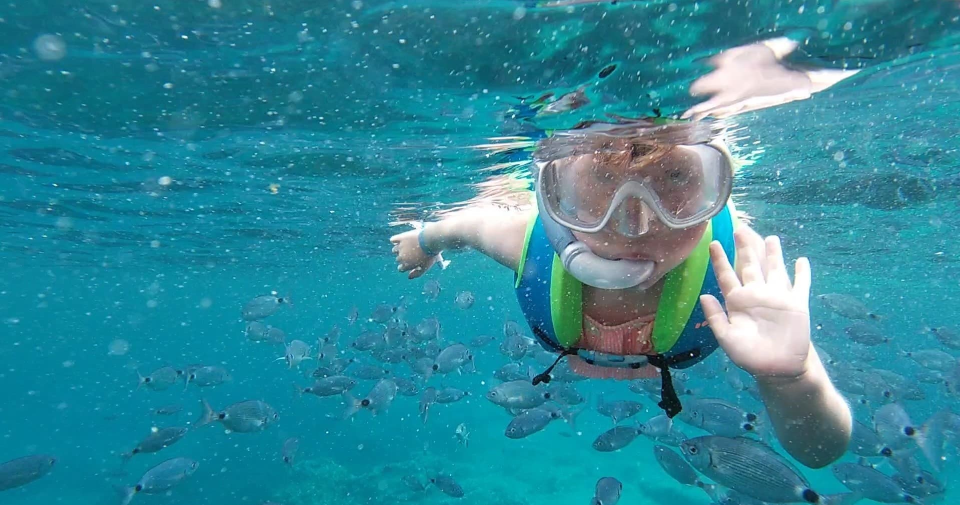 Child snorkeling underwater waving among tropical reef fish
