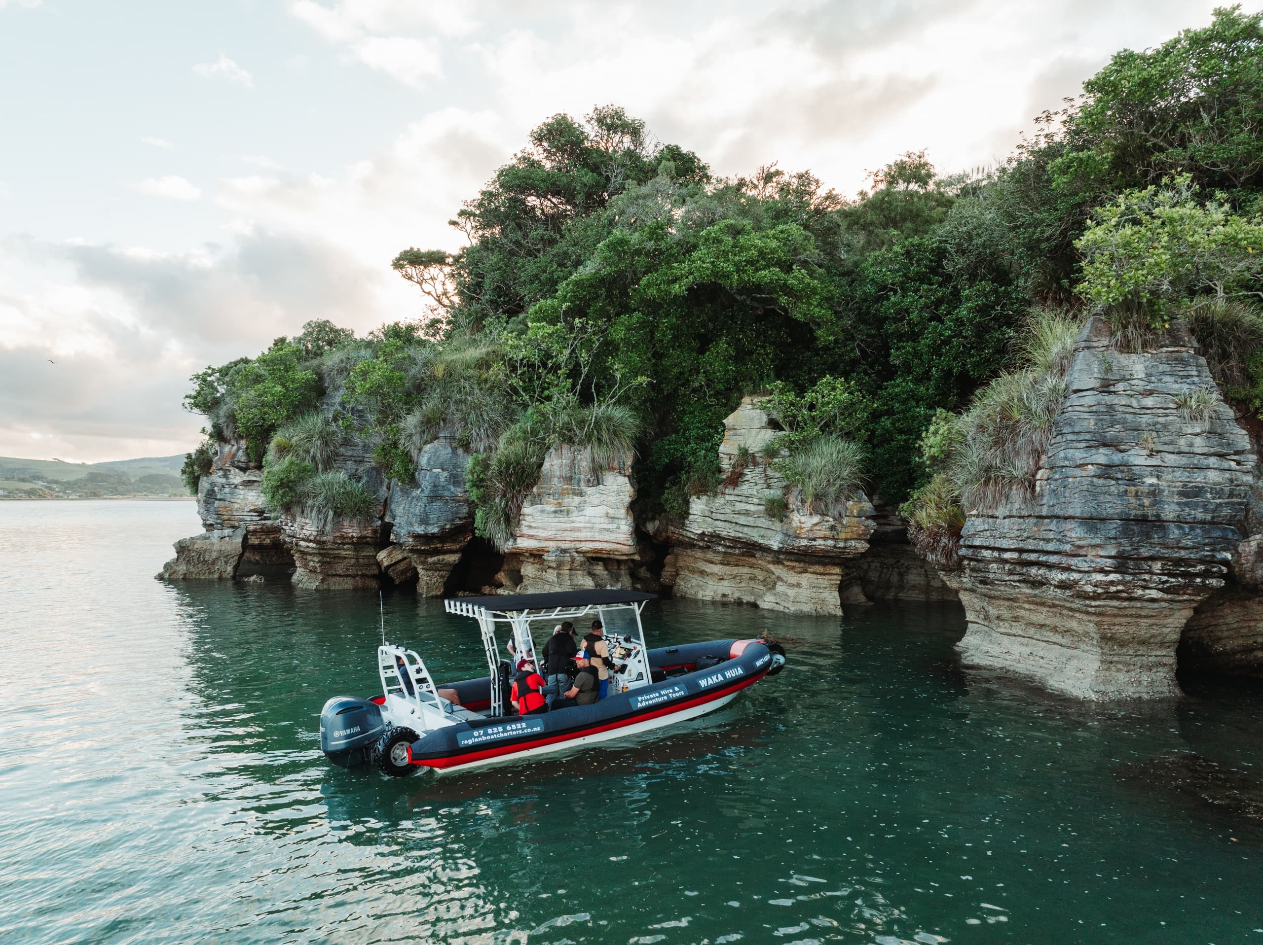 Rigid inflatable boat exploring coastal cliffs and sea caves in Raglan