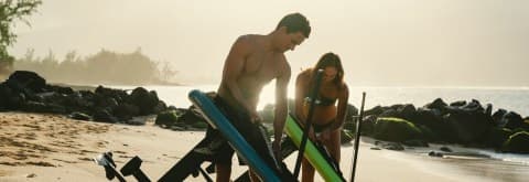 Couple preparing electric surfboards on sandy beach shoreline