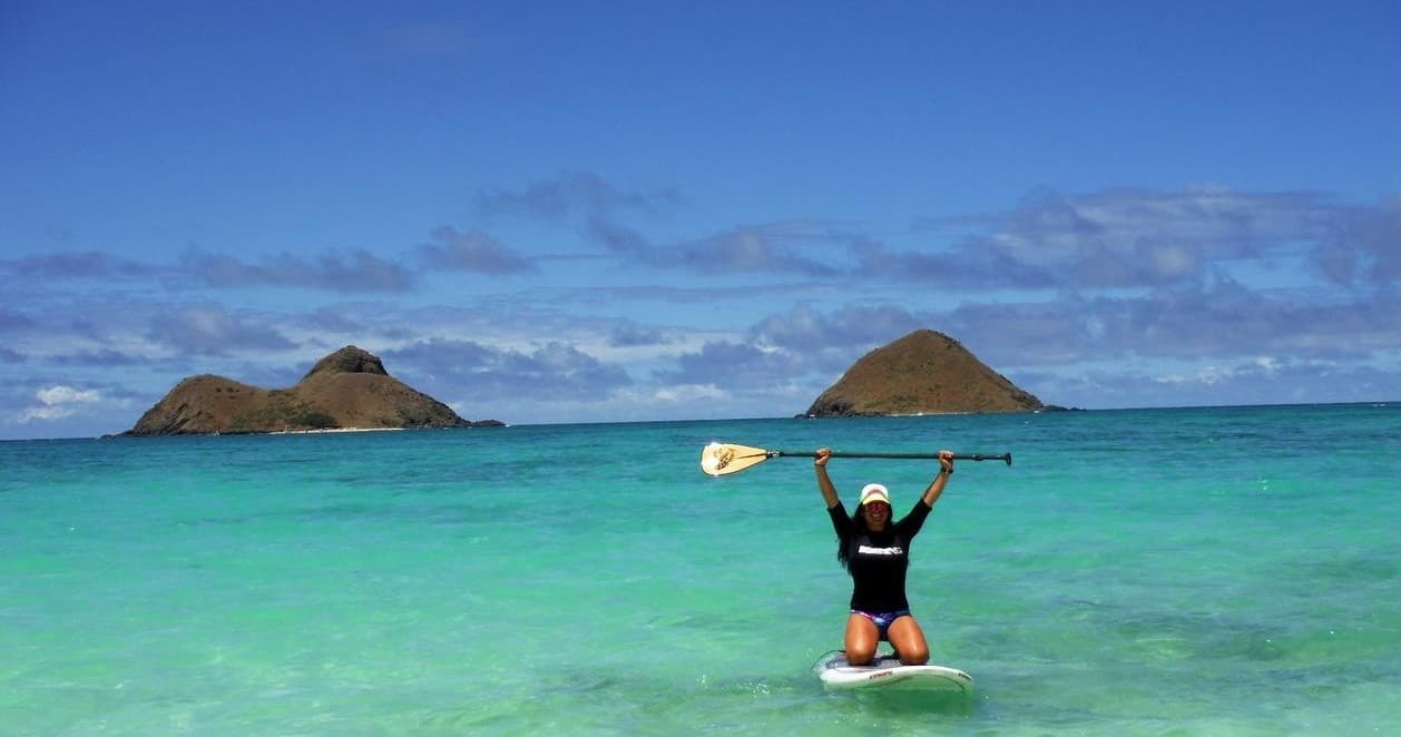 Paddleboarder celebrating in turquoise bay with islets near shore