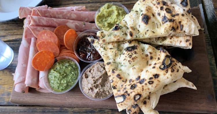 Charcuterie platter with flatbread and dips on wooden board in restaurant