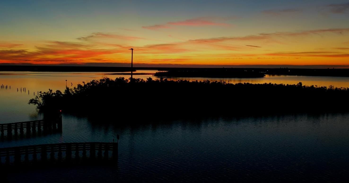 Sunset over calm mangrove estuary with silhouetted pier