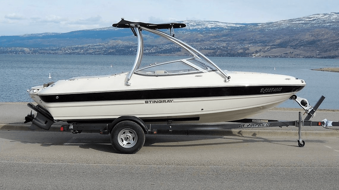 White bowrider parked lakeside with mountain views and trailer
