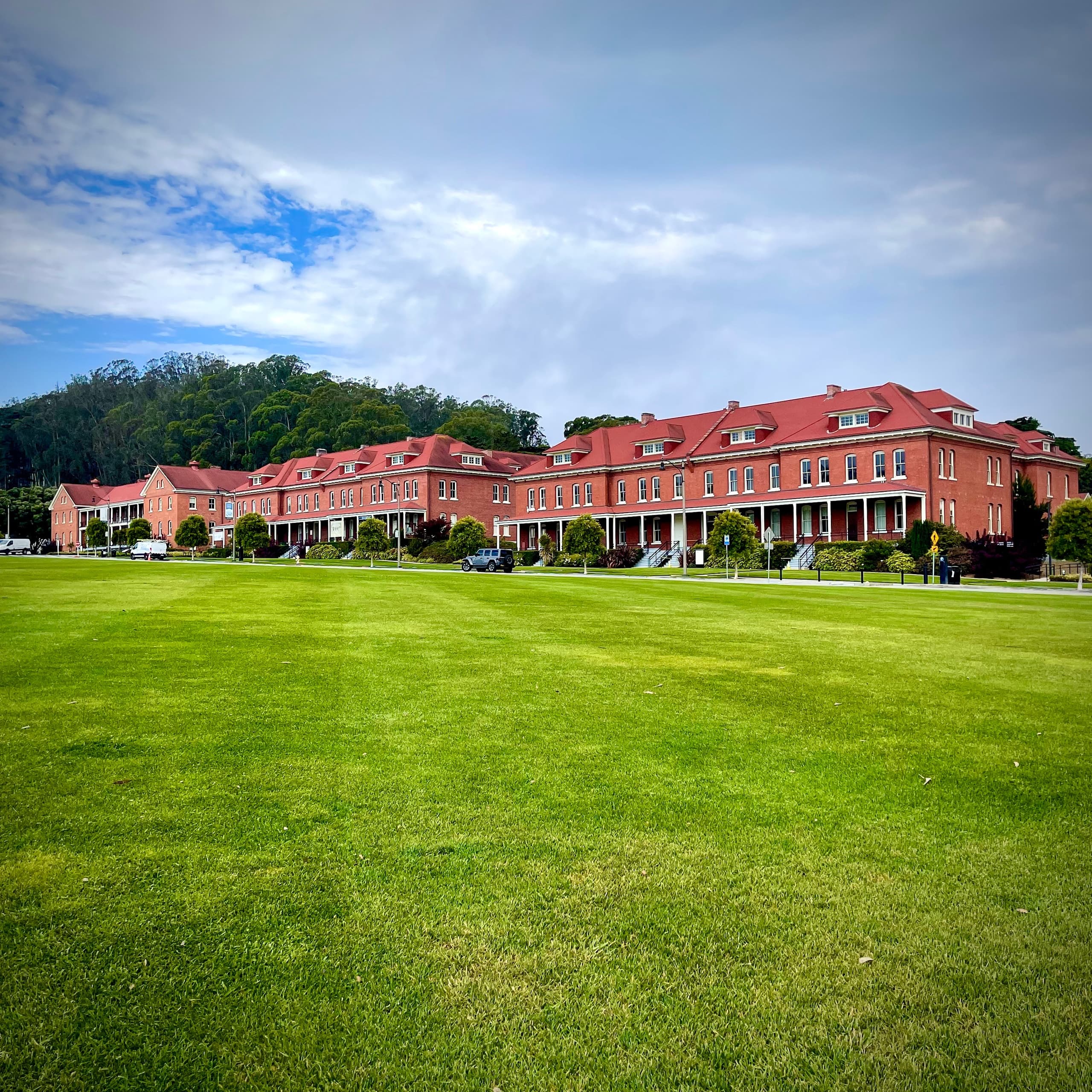 Walking tour across expansive grassy field by historic red-brick buildings