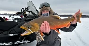 Angler holding trophy trout on frozen lake during ice fishing
