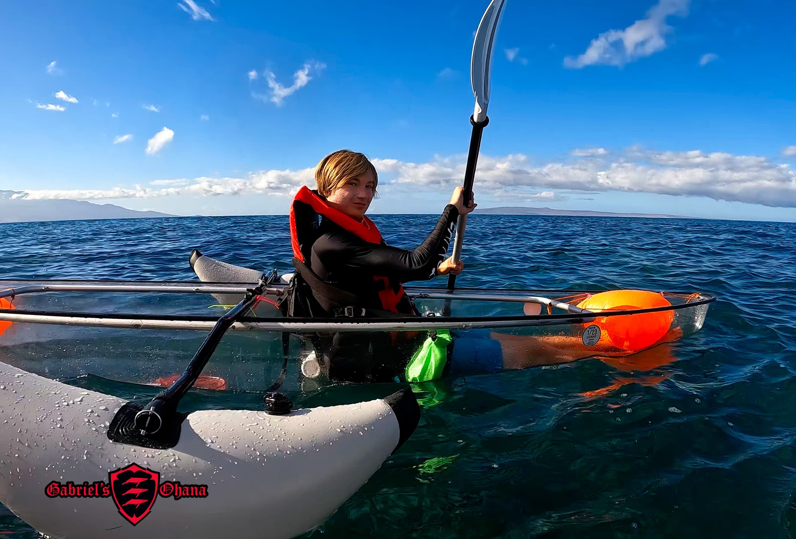 Solo paddler in transparent ocean kayak on bright sea