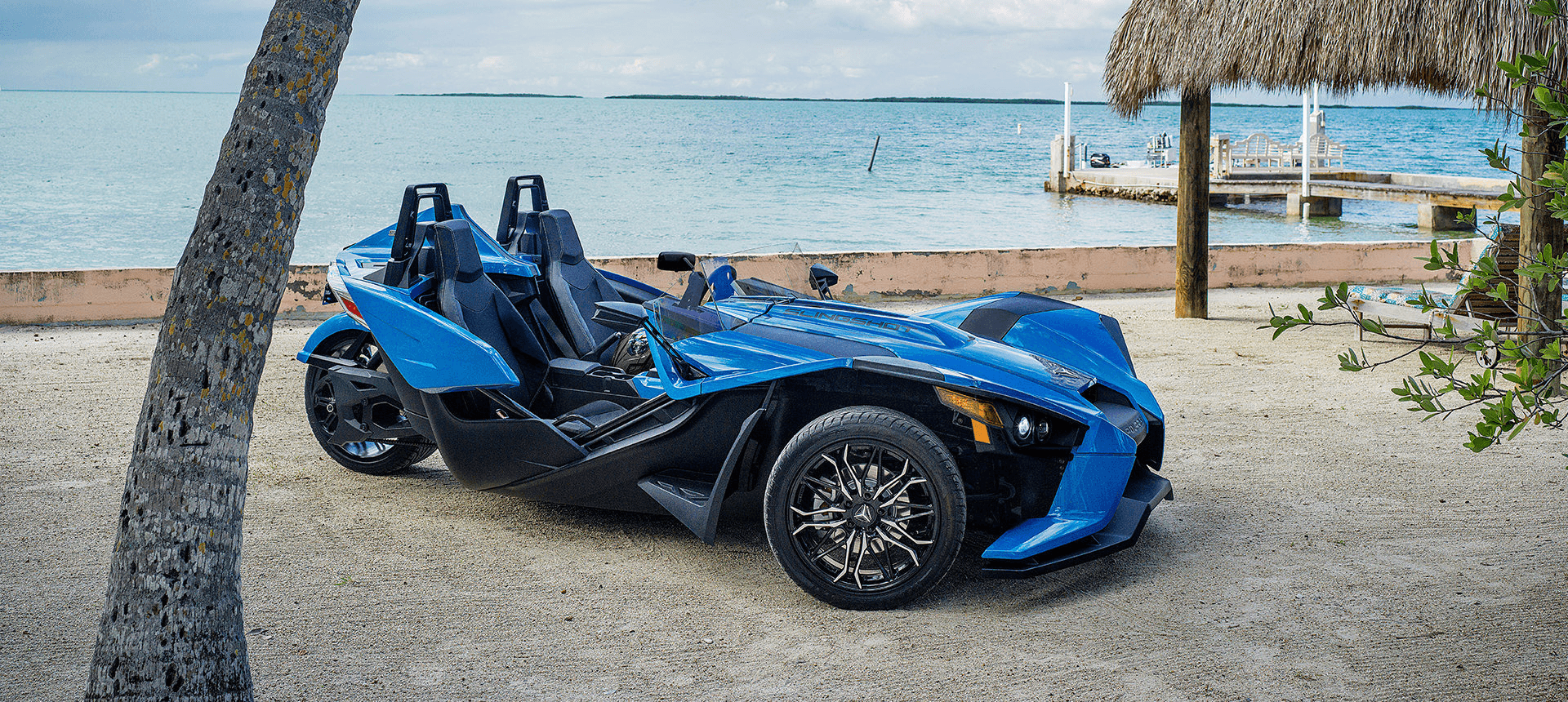 Blue two-seat Slingshot by palm trees on tropical beach