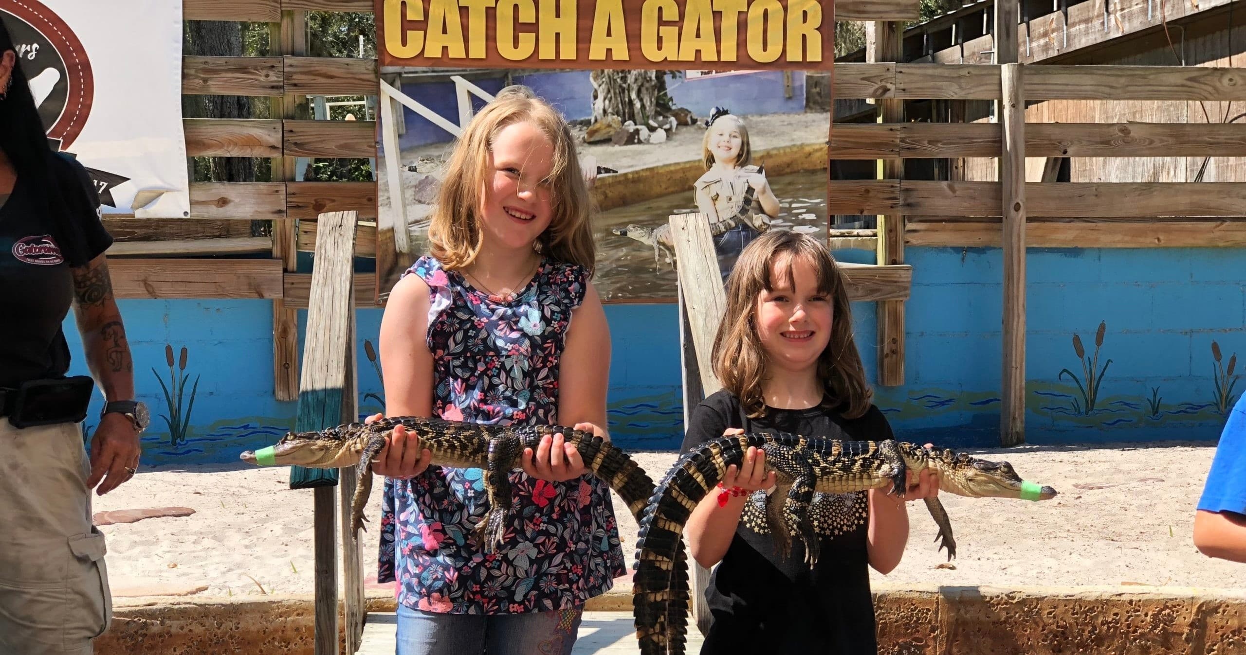 Children holding small alligator on outdoor farm stage at Gatorama
