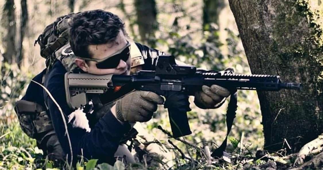 Camouflaged airsoft player aiming rifle in forest combat