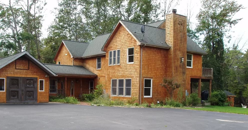 Wooden lakeside cabin rental surrounded by trees and driveway