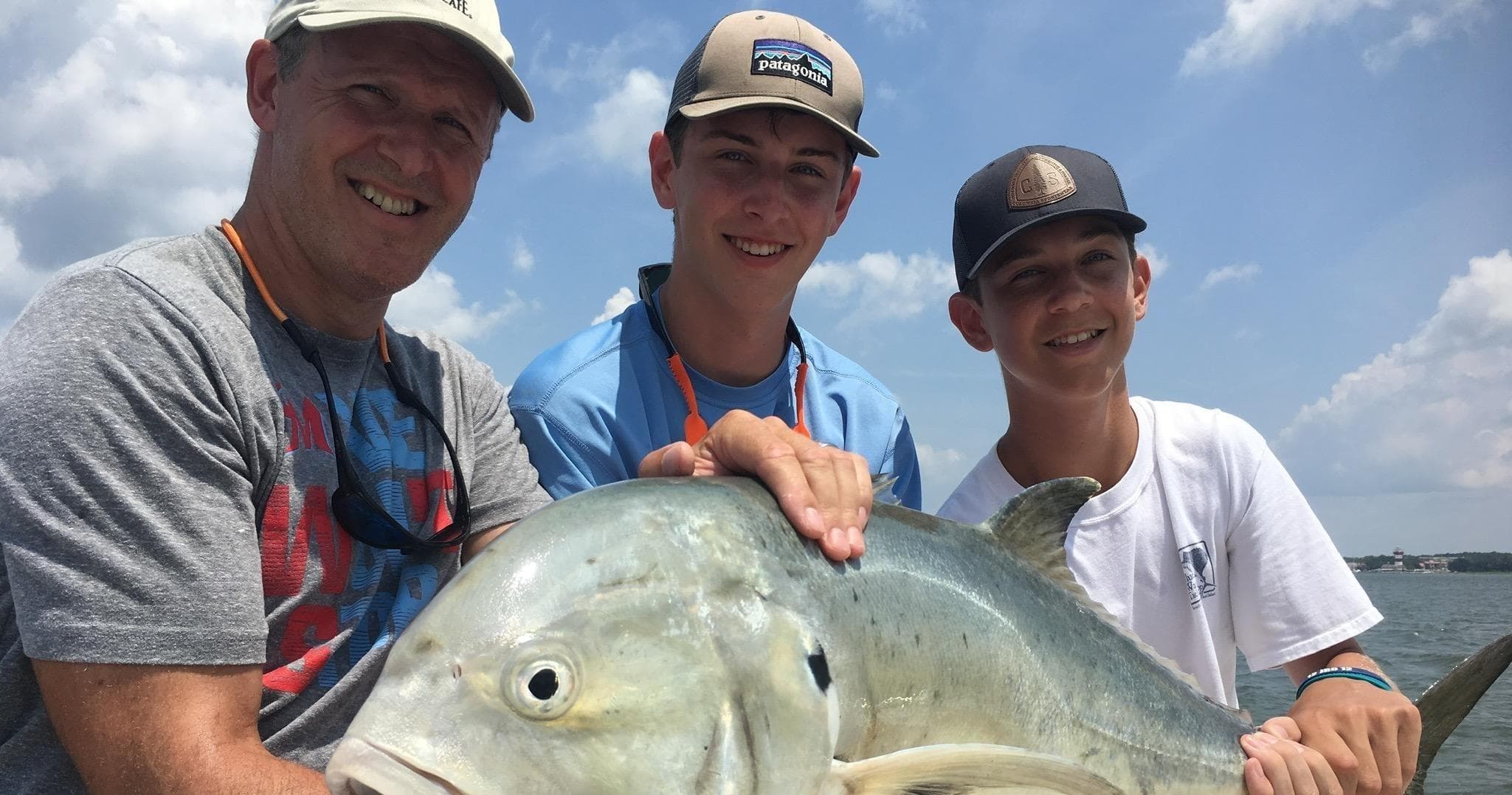 Three anglers holding large jack fish on boat in coastal waters