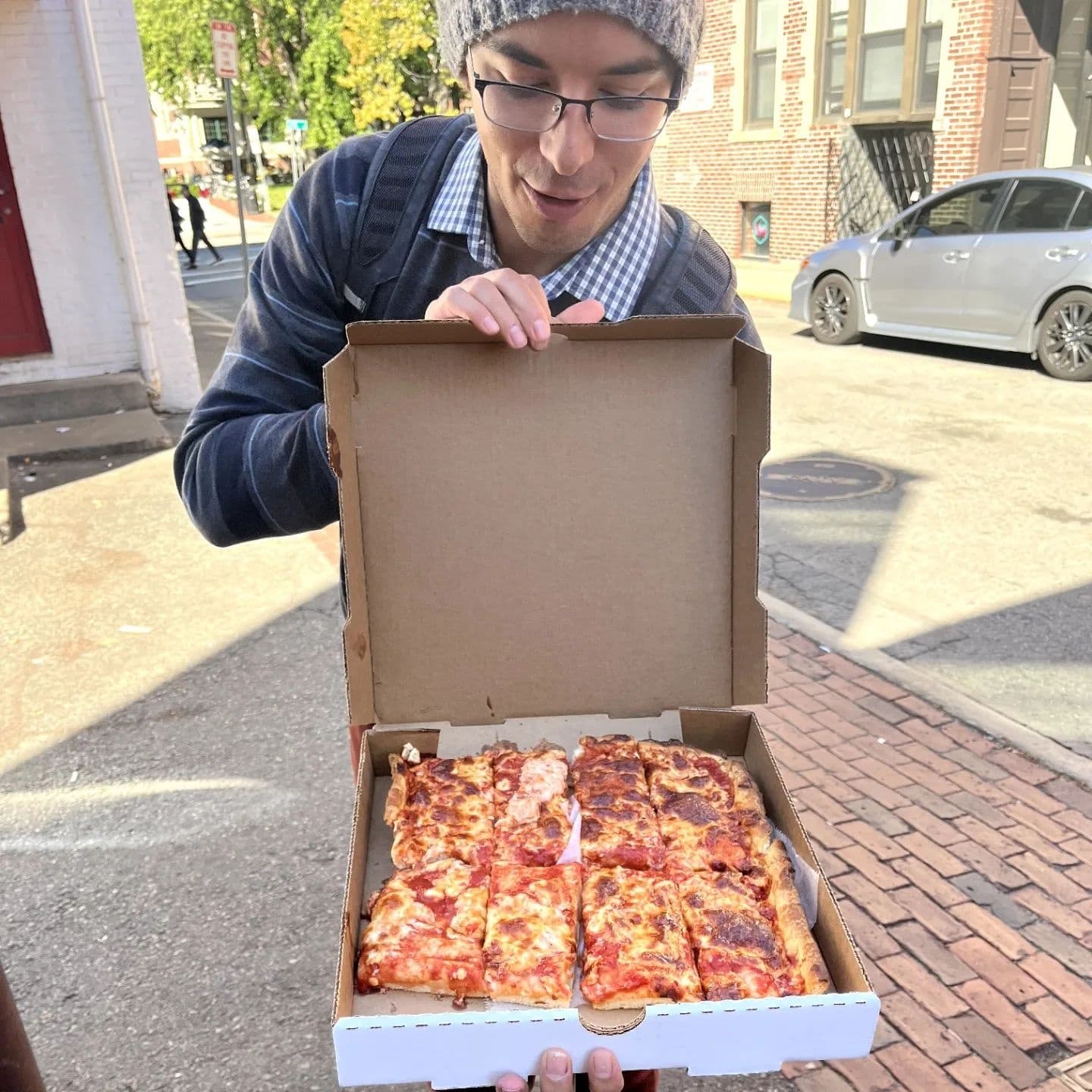 Guide holding local pizza box on city street, food walking tour