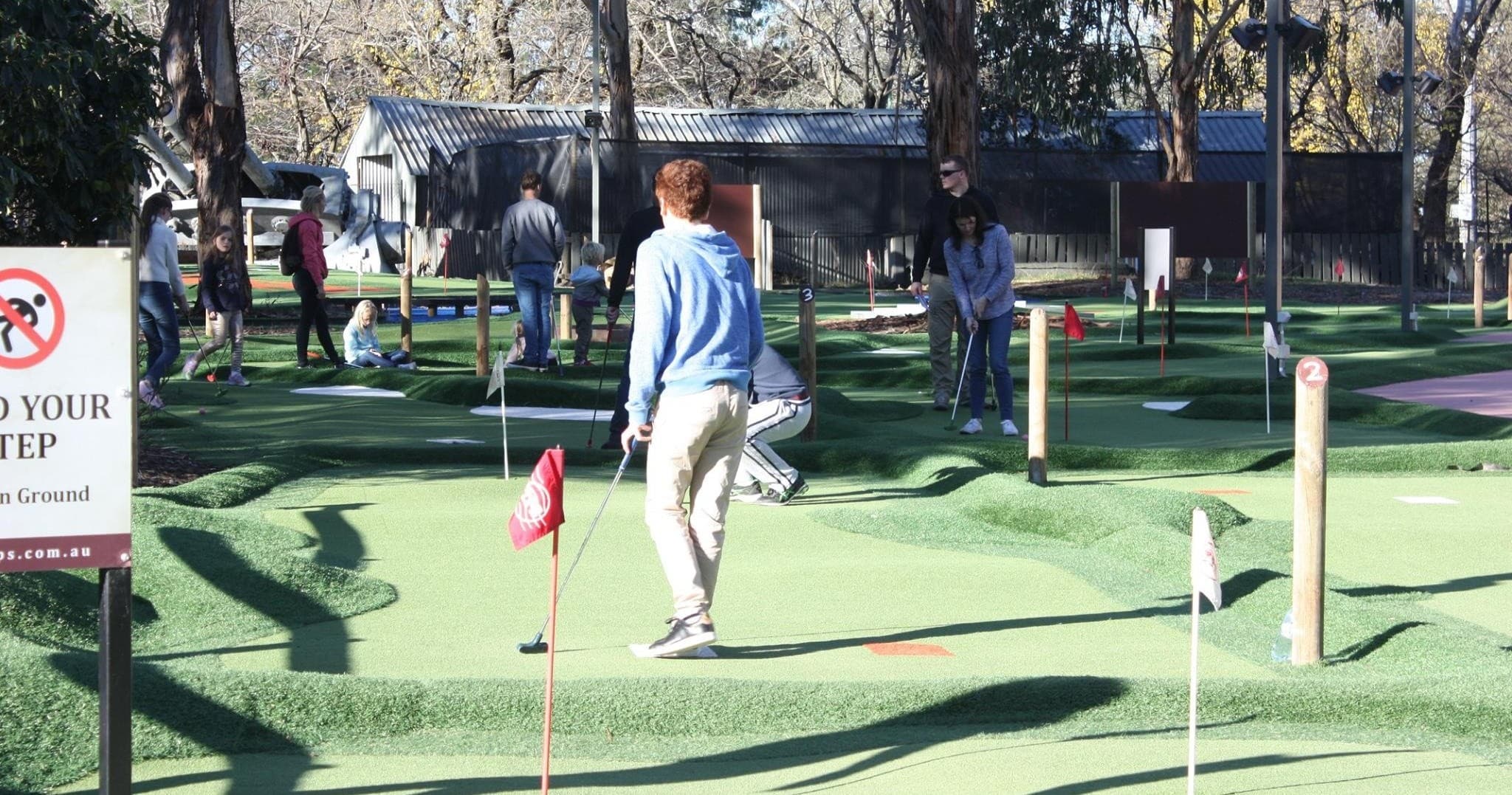 People playing outdoor mini golf on sunny course with flags