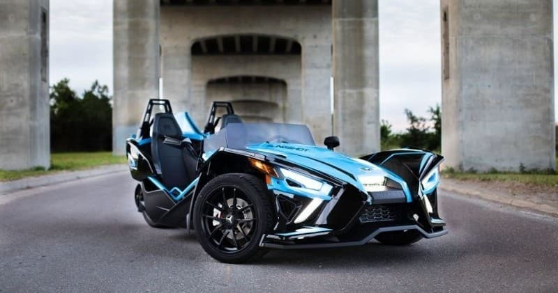 Blue three-wheeled sport roadster parked under urban bridge backdrop