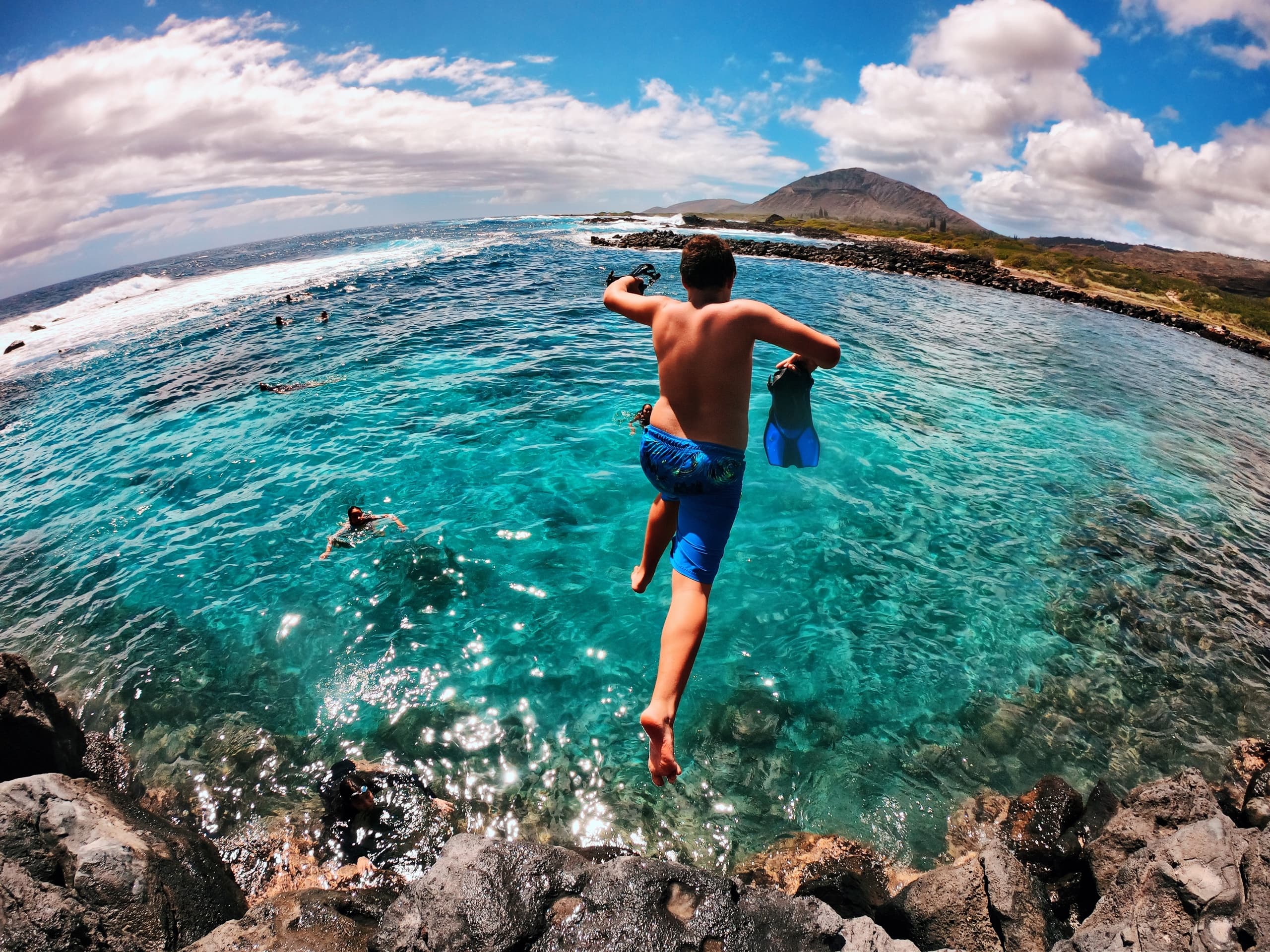 Cliff jumper leaping into crystal ocean from rocky shore