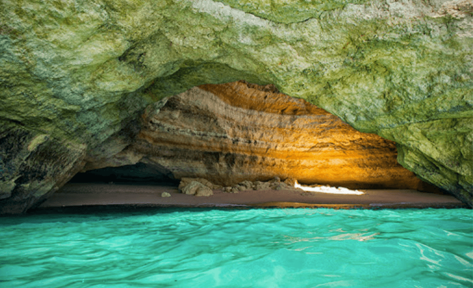 Sunlit sea cave with sandy inlet and emerald clear water for swimming