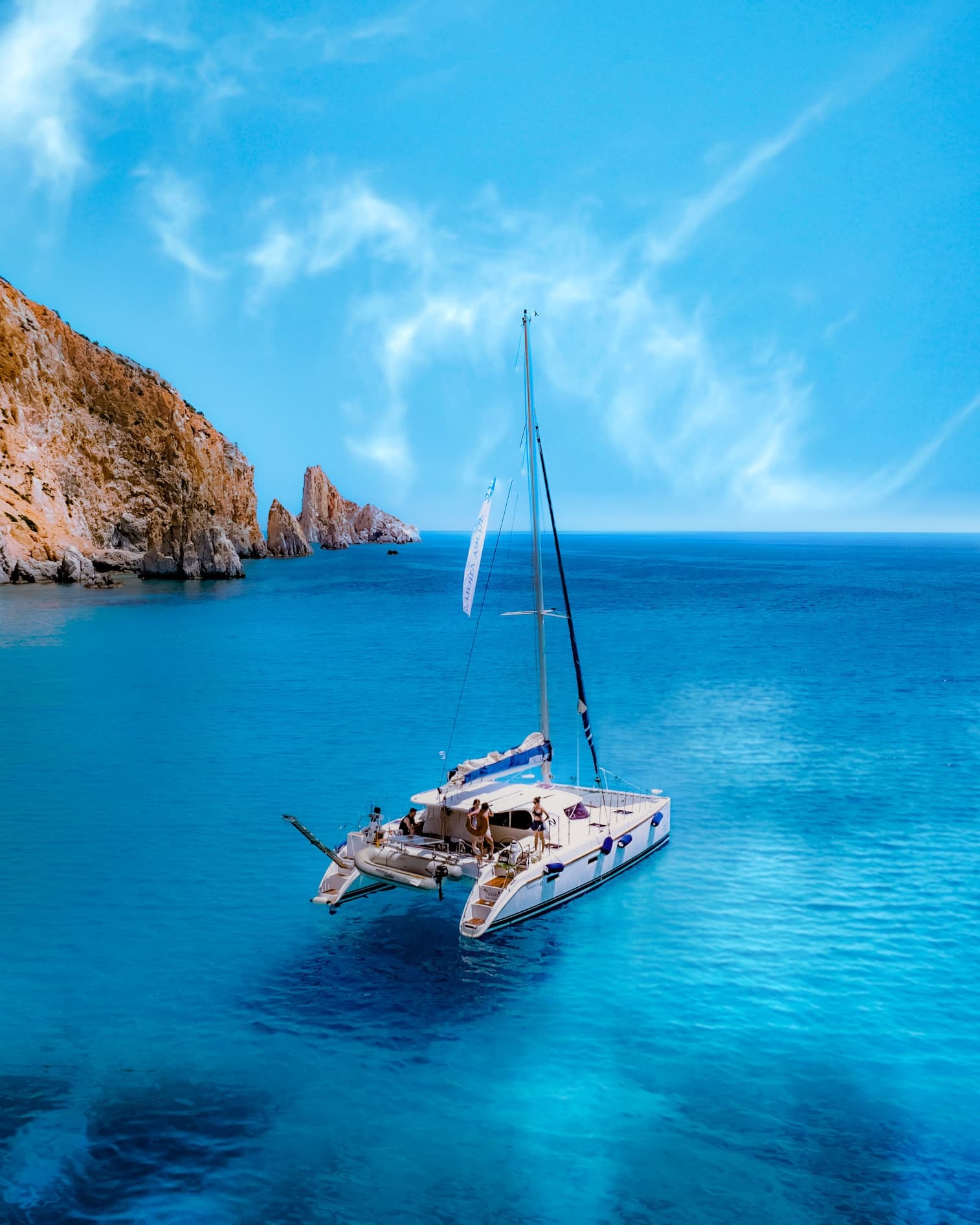 Sailboat anchored near rocky coastal cliffs in clear blue sea