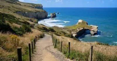 Hikers on coastal cliff path approaching sea arches and ocean