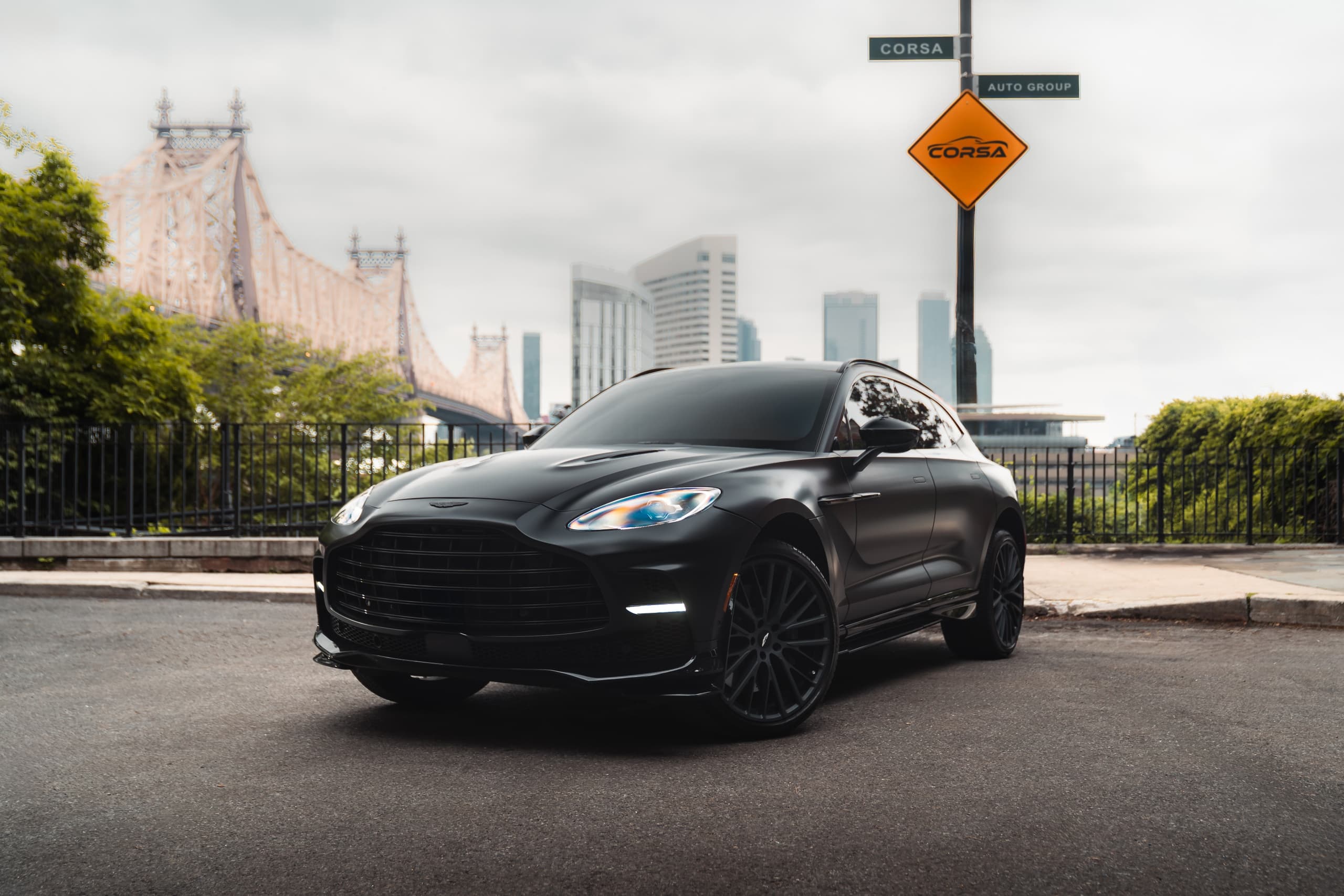 Black sports car parked by city bridge with skyline view