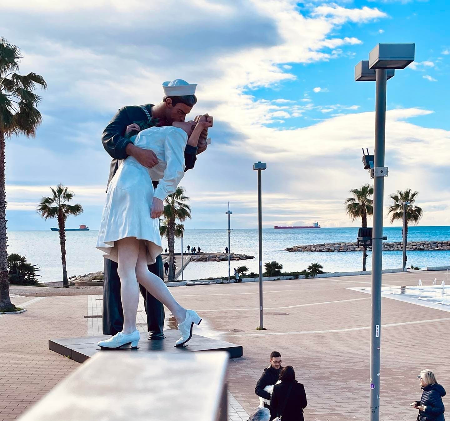 Seaside statue of sailor kissing partner with palm-lined promenade