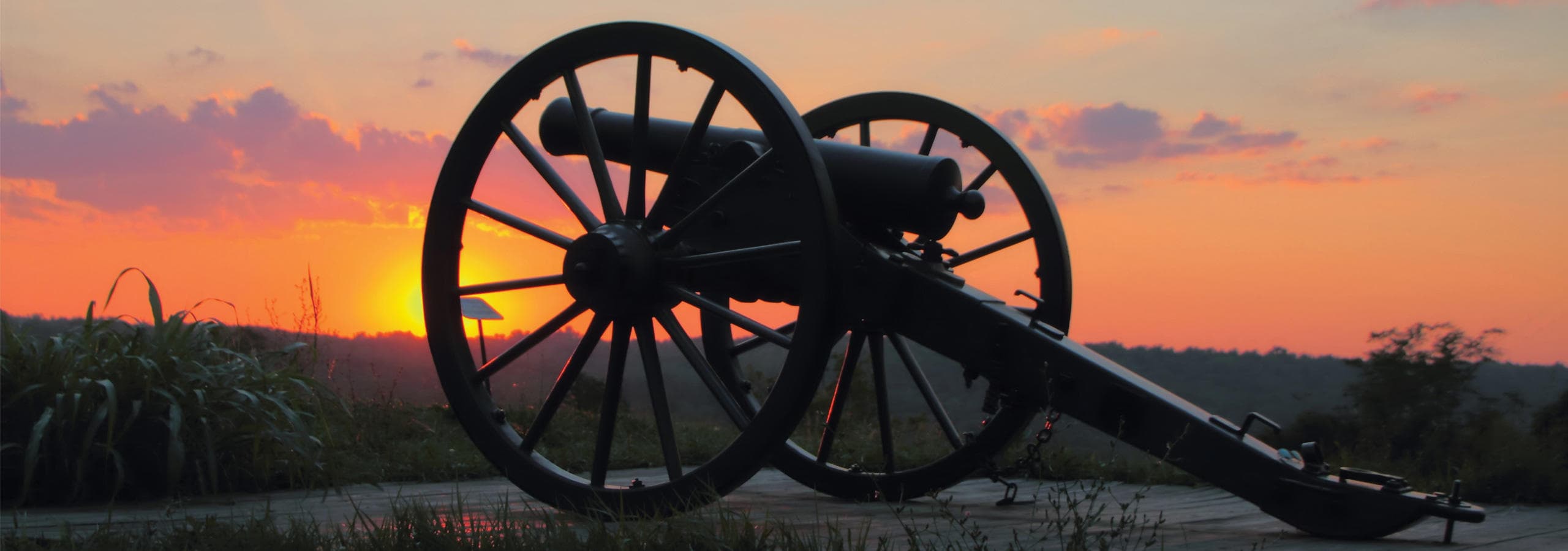 Civil War cannon silhouette at sunset on open battlefield