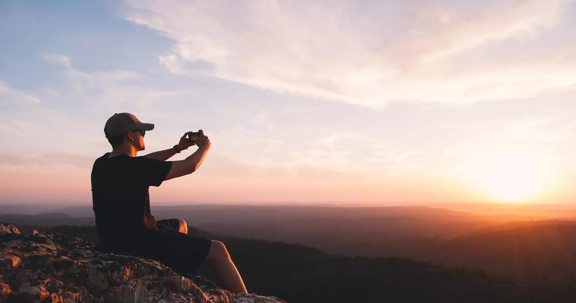 Photographer capturing sunset view from rocky hilltop overlook