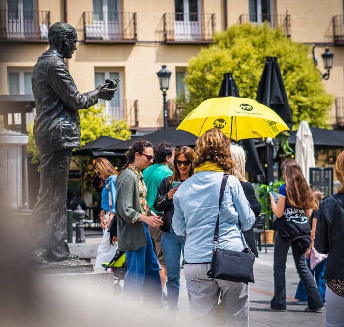 Guided walking tour around bronze statue with yellow umbrella in Madrid