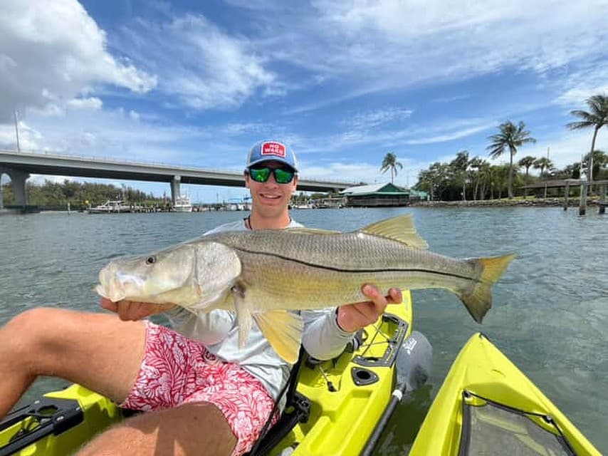 Angler holding large snook while seated in yellow kayak