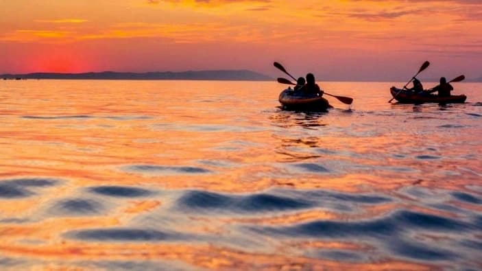 Two kayakers silhouetted at sunset over calm ocean horizon